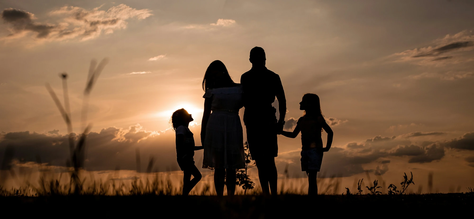 Familie mit zwei Kindern auf einem Feld bei Sonnenuntergang in ruhiger und verbundener Atmosphäre.